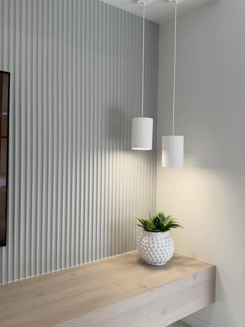 Full-height vertical feature panelling beside a floating timber surface and two pendant lights