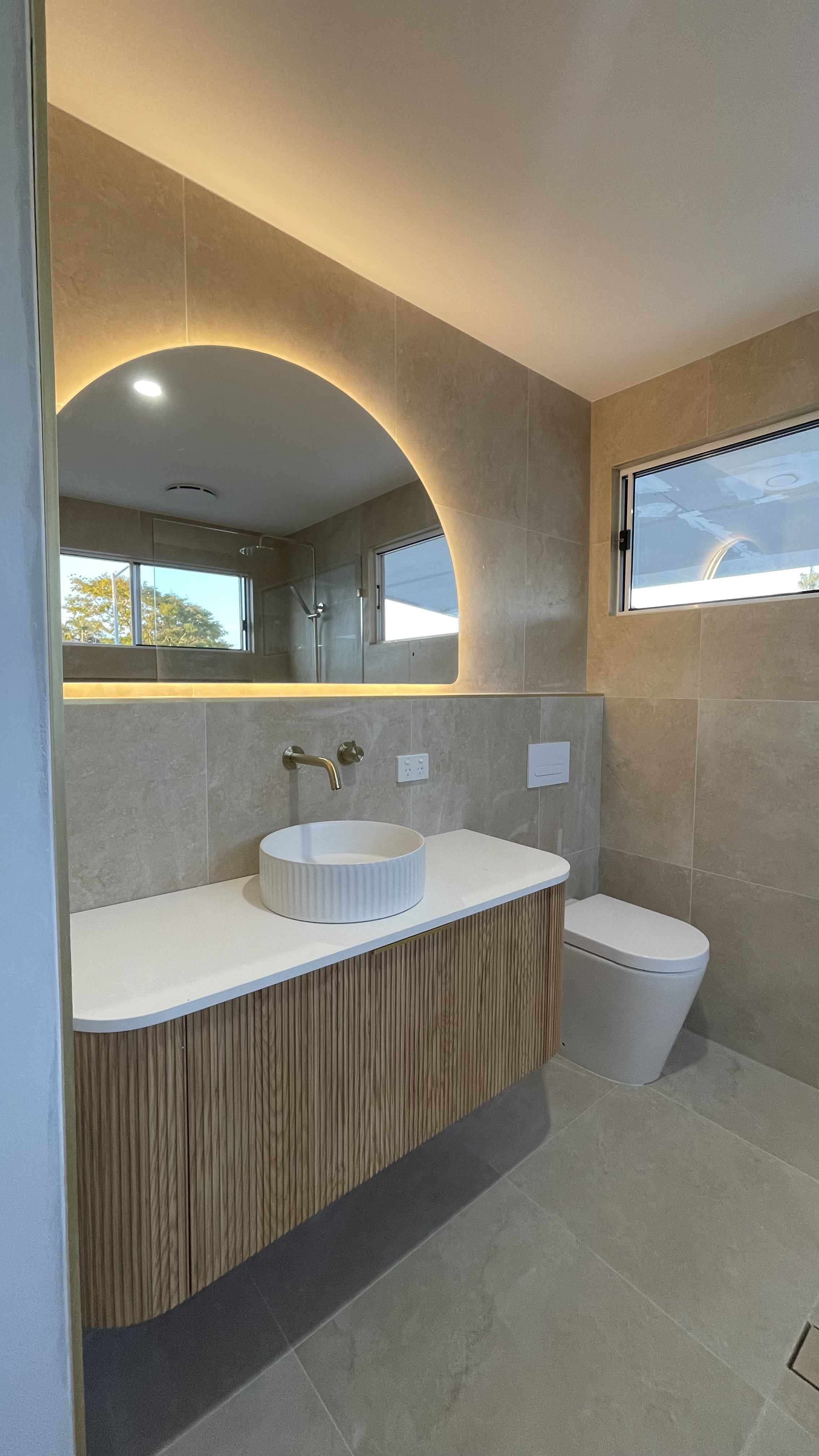 Renovated bathroom with arched backlit mirror, fluted timber vanity and brushed brass tapware